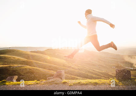 Mann springt über den Abgrund zwischen zwei Steinen auf Berge bei Sonnenuntergang Stockfoto