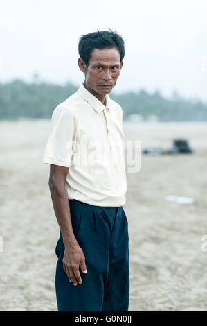 Applying Myanmar Mann mit schwarzen Haaren und einem gelben weißes T-shirt an einem Strand, Blick geradeaus in eine Kamera. Stockfoto