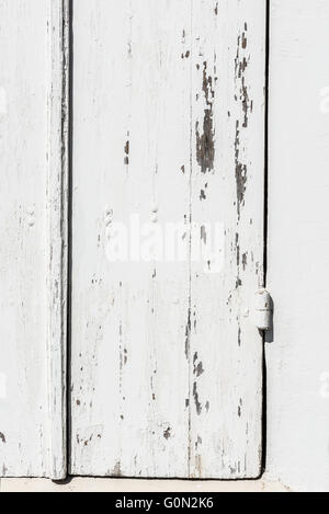 Verwitterte weiße Holztür mit Scharnieren mit weißer Farbe gesäumt und Peeling texturiert. Stockfoto