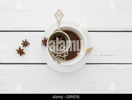 Tasse Tee mit einem Vintage Sieb und Sternanis auf weißem rustikalen hölzernen Hintergrund Stockfoto