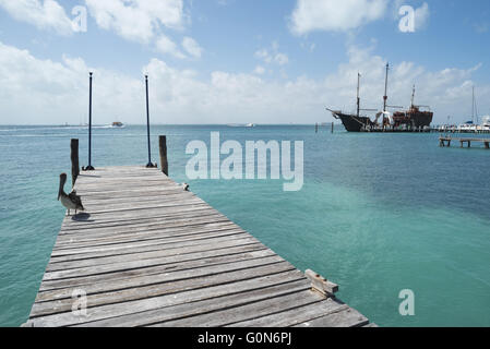 Karibik-Strand Landschaft, klaren, türkisfarbenen Wasser mit Pelikan Vogel auf hölzernen Pier Brücke und alte nautische Schiff in der Ferne. Stockfoto