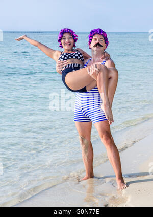 Mann im Badeanzug mit in seine Arme eine Frau im Badeanzug am Meeresstrand Stockfoto