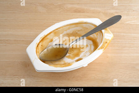 Eine TV-Diner-Mahlzeit, die mit einem Löffel in der Plastikschale auf einem Holztisch gegessen hat. Stockfoto