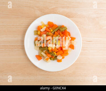 Draufsicht einer Portion gemischtes Gemüse auf einem weißen Teller oben auf einer hölzernen Tischplatte. Stockfoto