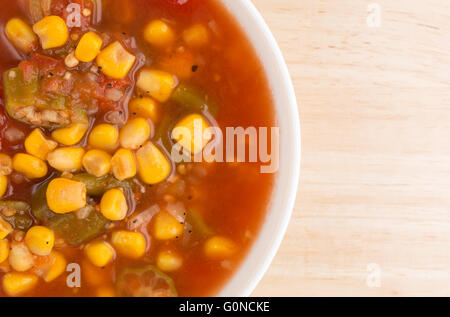 Top-Nahaufnahme von einer Schüssel gefüllt mit Mais, Okra und geschmorten Tomaten in Wasser mit Gewürzen auf einem Holztisch. Stockfoto