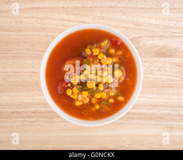 Draufsicht einer Schüssel gefüllt mit Mais, Okra und geschmorten Tomaten in Wasser mit Gewürzen auf einem Holztisch. Stockfoto