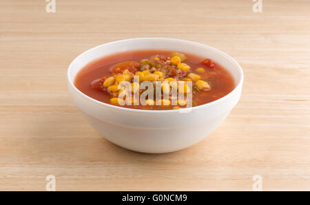 Seitenansicht einer Schüssel gefüllt mit Mais, Okra und geschmorten Tomaten in Wasser mit Gewürzen auf einem Holztisch. Stockfoto