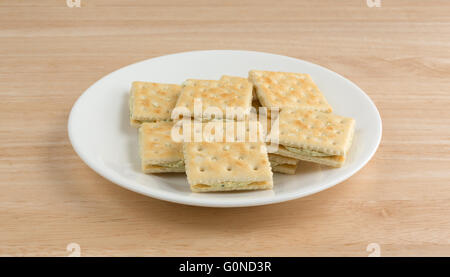 Seitenansicht der Frischkäse und Schnittlauch Cracker auf einem weißen Teller oben auf einer hölzernen Tischplatte. Stockfoto