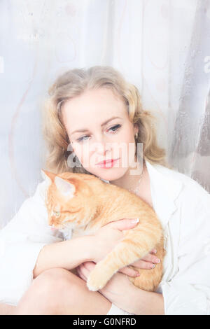 Schöne Frau am Fenster mit einer roten Katze an ihren Händen Stockfoto