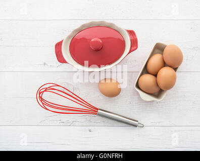 Rote Hand Schneebesen mit Eiern und Schüssel auf einem weißen Hintergrund Holz Stockfoto