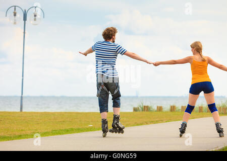 Urlaub, aktive Menschen und Freundschaft Konzept. Junge passen paar auf Rollschuhen fahren im Freien am Meer Ufer, Frau und Mann zusammen auf der Promenade Inlineskaten Stockfoto