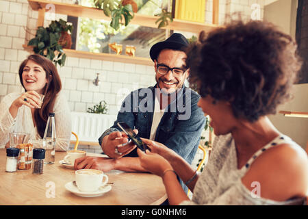 Porträt der jungen Freunde sprechen im Café und betrachten der Fotos auf Smartphone. Glückliche junge Menschen, die eine tolle Zeit bei einem Stockfoto