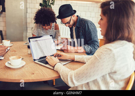 Porträt der jungen Frau, die mit ihren Freunden in einem Café sitzen am Laptop arbeiten. Freunden an einem Tisch im Café sitzen. Stockfoto