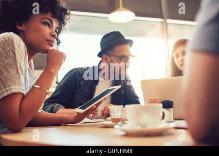 Porträt von Afrikanerin mit digital-Tablette und Menschen im Hintergrund an einem Cafétisch hautnah. Junge Freunde sitzen an einem cof Stockfoto