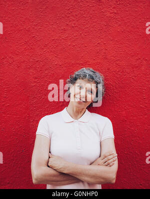 Porträt von schöne Reife Frau, die Arme gekreuzt vor rotem Hintergrund stehend. Stockfoto