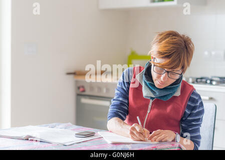 Frau mit Brille sitzt am Tisch, Lesung und Handschrift Papiere und Dokumente. Tiefenschärfe, Inneneinrichtungen. Concep Stockfoto