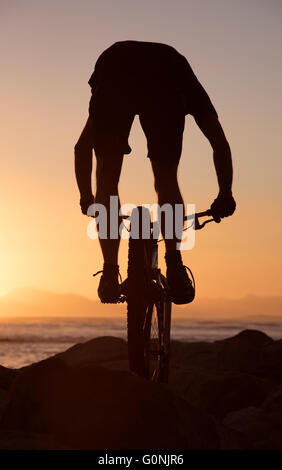 Silhouette von einem Mountain-Bike-Fahrer springen über Felsen auf der Strand in der Western Cape Südafrika bei Sonnenuntergang. Stockfoto