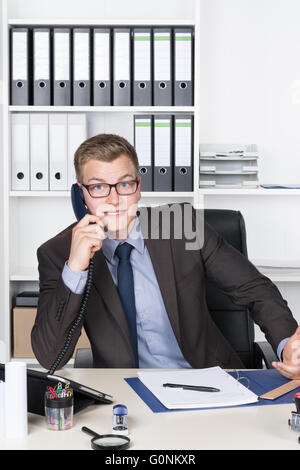 Junger Geschäftsmann mit Brille und ein schockiert, erstaunten Gesichtsausdruck ist telefonieren, beim Sitzen am Schreibtisch im Büro. A Stockfoto