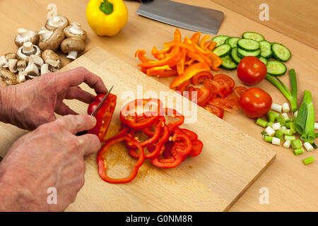 Nahaufnahme Schuss aus einem Köche Hände Ring schneiden eine gereinigte rote Paprika auf ein Schneidbrett aus Holz zur Seite eine Auswahl an gemischten Schnitt Stockfoto
