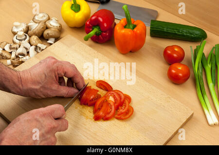 Nahaufnahme einer Köche Hände schneiden Salat Tomate auf ein Schneidbrett aus Holz zur Seite eine Auswahl an geschnittenen Mischgemüse Stockfoto