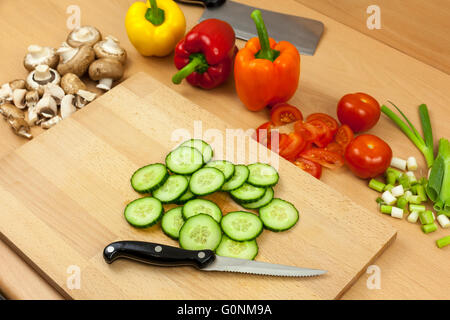 Frisch englische Gurkenscheiben auf ein Schneidbrett aus Holz mit einem Messer beiseite legen schneiden einige gemischte Gemüse Stockfoto