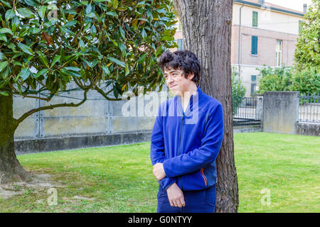 kleiner Junge lächelt lehnte sich gegen den Baumstamm Catalpa im Garten Stockfoto