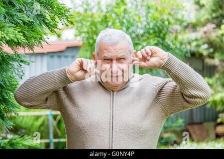 Ältere kaukasischen im grünen Garten erstreckt sich seine Ohren mit den Fingern nicht zu hören Stockfoto