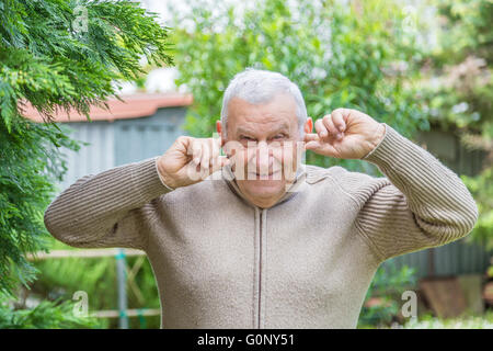 Ältere kaukasischen im grünen Garten erstreckt sich seine Ohren mit den Fingern nicht zu hören Stockfoto