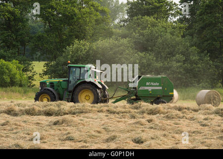 Silageherstellung - Bauernhof Traktor ziehen eine Rundballenpresse arbeitet auf einem Feld am großen Ouseburn, North Yorkshire, England. Stockfoto