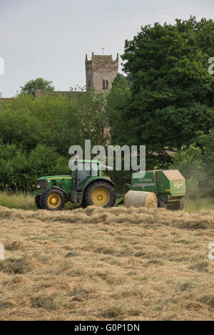 Silage oder Heu machen - der Mensch ist das Fahren Green Farm Tractor Pulling einer Rundballenpresse, die in einem Feld - Great Ouseburn, North Yorkshire, England, UK. Stockfoto