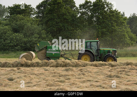 Great Ouseburn, North Yorkshire, GB-zylindrischen Ballen von Fallen, Rundballenpresse, gezogen von Farm Traktor fahren & Arbeiten in einem Feld, dass Silage. Stockfoto