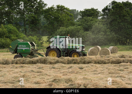 Green Farm Traktor arbeitet im Feld, Silage oder Heu machen, ziehen Rundballenpresse (4 zylindrischen Ballen darüber hinaus) - Great Ouseburn, North Yorkshire, GB. Stockfoto