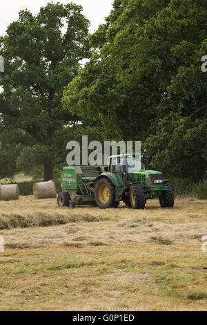 Silage machen, große Ouseburn, North Yorkshire, England - Bauernhof-Traktor in einem Bereich arbeiten, ziehen eine Ballenpresse mit Rundballen darüber hinaus. Stockfoto