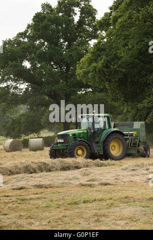 Heu oder Silage, Great Ouseburn, North Yorkshire, England, UK-Green Farm Traktor in einem Feld, das Ziehen einer Ballenpresse mit Rundballen darüber hinaus. Stockfoto