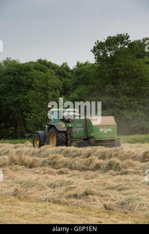 Heu oder Silage, - grün, farm Tractor Pulling Rundballenpresse, Fahren & hart arbeiten in Feld am Great Ouseburn, North Yorkshire, England, UK. Stockfoto