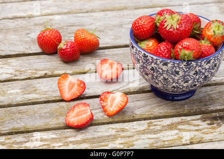 in Scheiben geschnitten und ganze Erdbeeren neben einer chinesischen Stil Schüssel auf einem Holztisch Garten Stockfoto