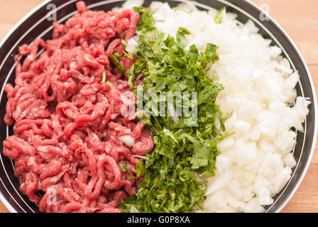 Rohes Hackfleisch mit fein gehackten frischen Grüns und Zwiebeln in einer Schüssel-Nahaufnahme. Stockfoto