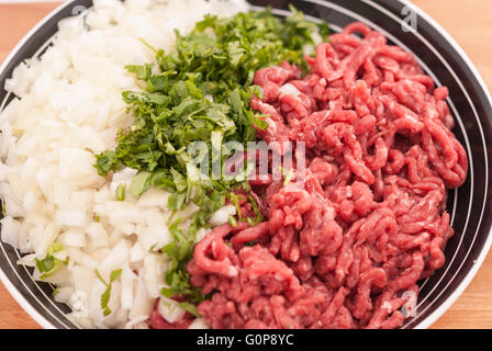 Rohes Hackfleisch mit fein gehackten frischen Grüns und Zwiebeln in einer Schüssel-Nahaufnahme. Stockfoto