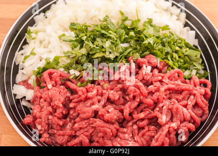 Rohes Hackfleisch mit fein gehackten frischen Grüns und Zwiebeln in einer Schüssel-Nahaufnahme. Stockfoto