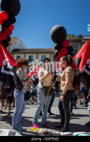 Junge Frauen reden zusammen mit schwarzen und roten Luftballons und Fahnen, wie Arbeitnehmer versammeln, um in Sevilla am 1. Mai 2016 protestieren Stockfoto