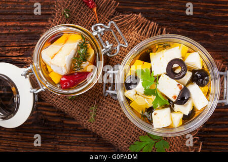 Marinierter Camembert und griechischen Kunststück Käse in Öl in Glas auf Holztisch. Traditionelle kulinarische Käse essen. Stockfoto