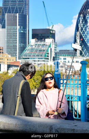 Frau Tourist auf Tower Bridge Bürgersteig komponieren ein Foto per Selfie-Stick und Smartphone mit der Londoner Skyline-Blick über England UK Stockfoto