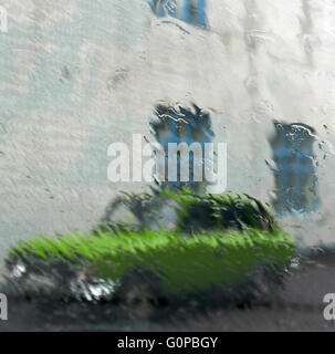 Muster von Wasser dampft auf Fensterglas bei Regen mit grünen Auto und Gebäudewand mit blauen Fenstern außerhalb Stockfoto