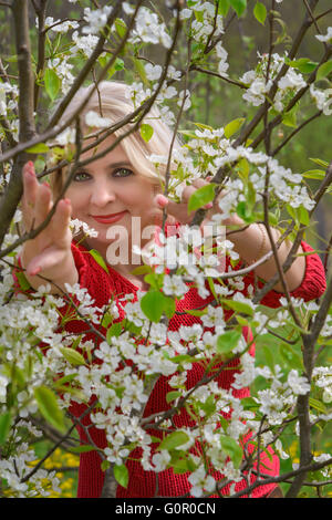 Schöne Blondine mittleren Alters wird zwischen den Zweigen der Apfelblüte fotografiert. Stockfoto