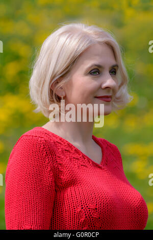 Blondine in einen roten Pullover wird auf einem Hintergrund von blühenden Löwenzahn fotografiert. Stockfoto