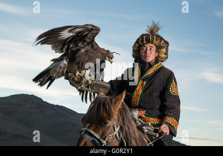 Mann in traditioneller Kleidung, auf einem Pferd einen Steinadler auf dem Arm halten Stockfoto