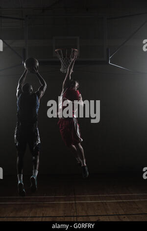 Basketball-Spieler schießen einen Basketball mit einem Verteidiger Stockfoto