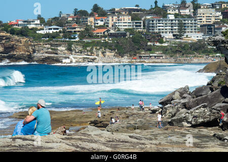 Menschen sitzen auf den Felsen am Rand des Ozeans in Tamarama, Sydney. Stockfoto