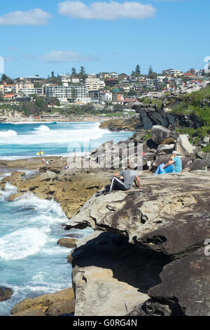 Menschen sitzen auf den Felsen am Rand des Ozeans in Tamarama, Sydney. Stockfoto