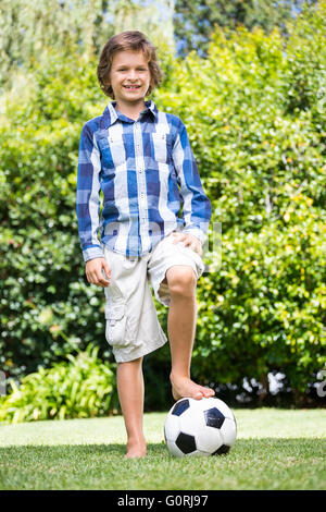 Süsser Boy Lächeln und posieren mit seinem Fuß auf einem Fußball Stockfoto